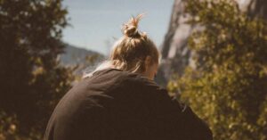 Back view of a woman sitting in the forest at the foot or a mountain