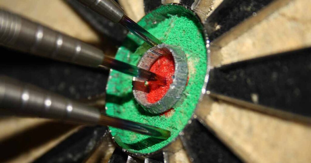 Close up of the bullseye on a dart board with 3 darts sticking into it