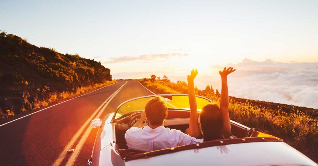 Couple in a convertible car driving on a road in the mountains at sunset