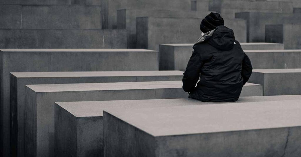 Back view of a person in a hoodie and jacket sitting on concrete blocks