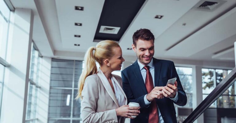 Man and woman looking at a mobile phone standing in an office