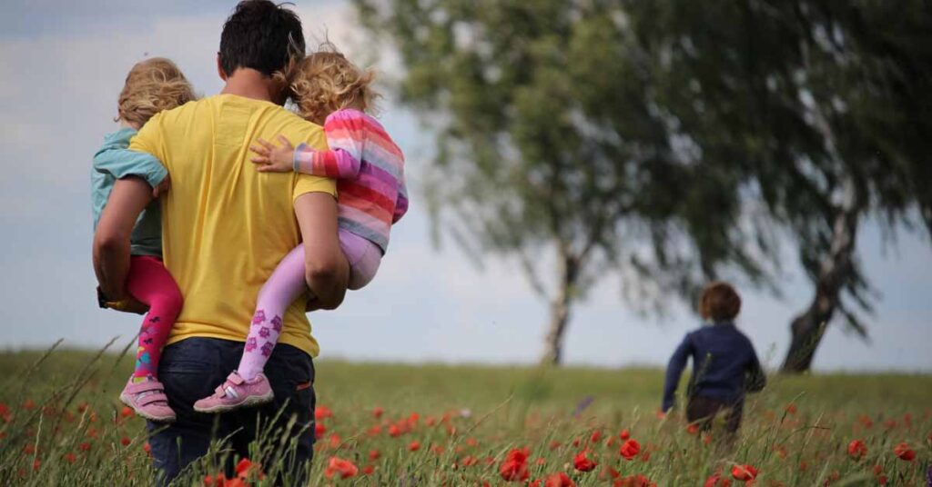 Man holding children in his arms while walking through a poppy field chasing a boy