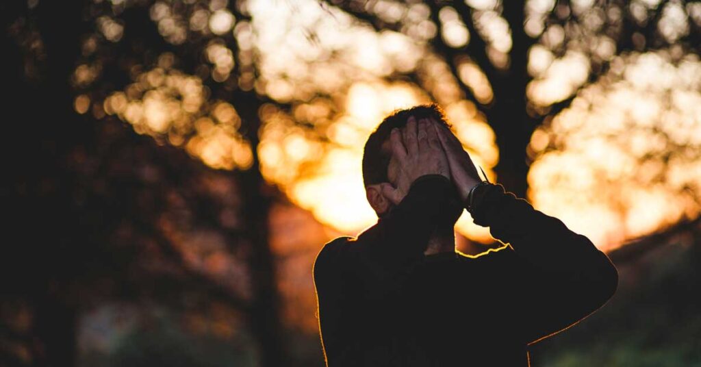 Man at sunset in a forest with hands over his face