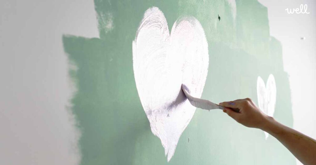 Close up view of a hand painting a white heart shape onto a green painted wall
