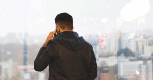 man standing in front of a window in an office on the phone in casual clothes