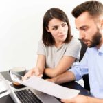 Couple looking at a laptop with paperwork in front of them