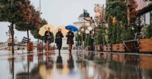 Rainy day street view with three people walking with umbrellas