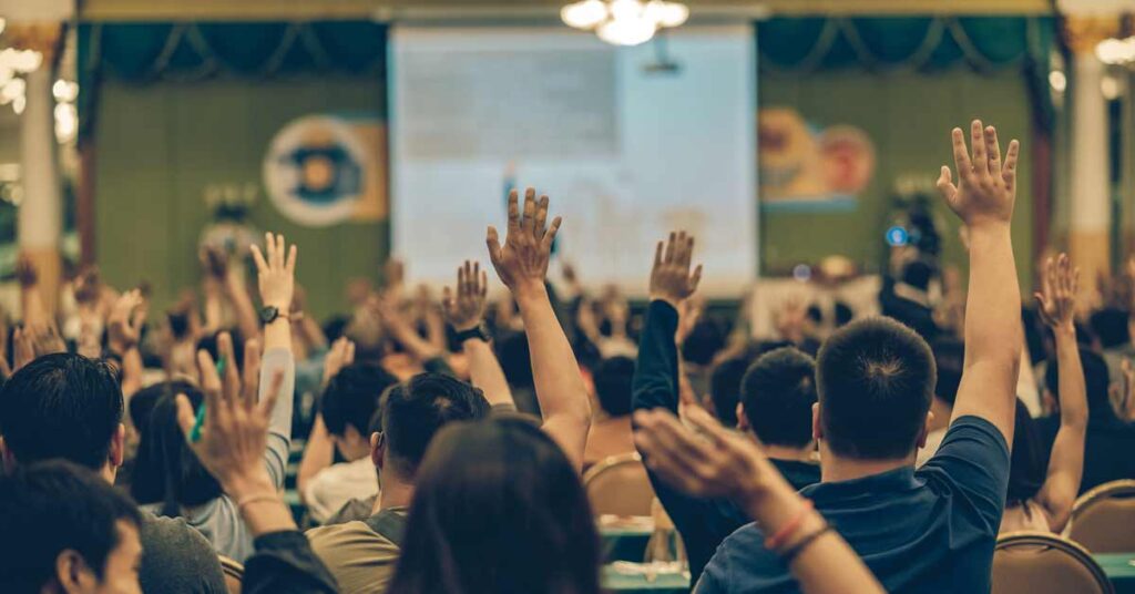 Rear view of an audience at a conference with their hands raised to ask questions