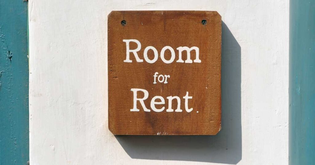 Wooden block sign screwed onto a wall with writing saying Room for Rent