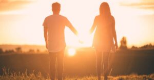 Rear view of a young couple holding hands looking out at a sunset