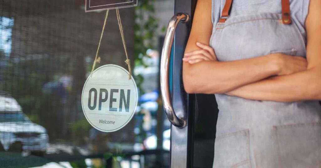 Close up of a person with crossed arms standing in front of an open sign of a business door