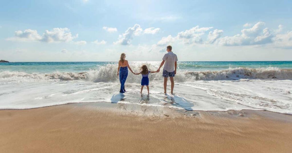 Family with child between man and woman holding hands at the beach in front of the waves