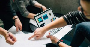 Person pointing to ideas on a piece of paper while stiting a desk in front of a laptop